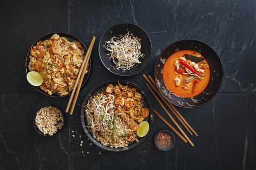 Authentic classic Pad Thai with shrimps. Fried rice with chicken. Thai Tom Yum soup.  Flat lay top-down composition on dark background.