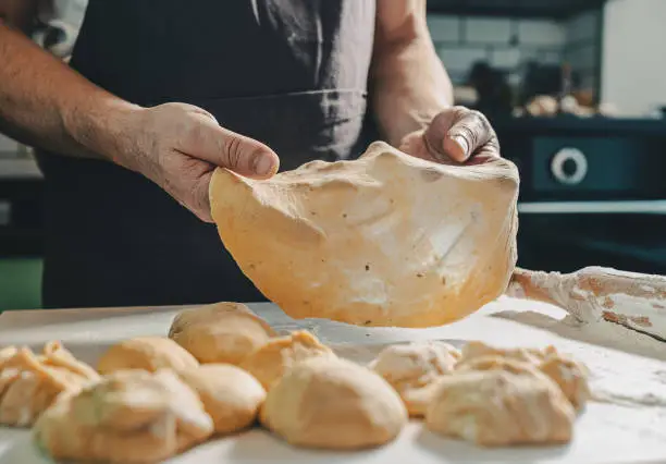 muscular hands of male baker hold thinly rolled dough. man prepares homemade cakes, on table there is dough, spilled flour and kitchen utensils