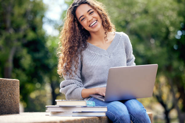 ritratto ritagliato di un'attraente giovane studentessa che usa il suo laptop per studiare fuori nel campus - studente universitario foto e immagini stock