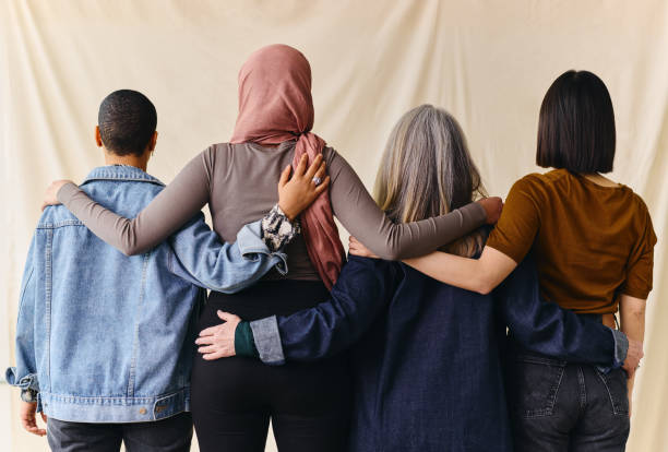 Rear view of four women with arms around each other in support of International Women's Day Rear view of four women with arms around each other in support of International Women's Day arm around stock pictures, royalty-free photos & images