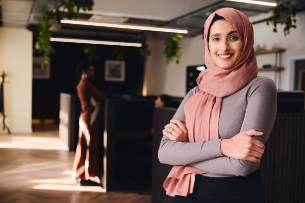 portrait of confident young middle eastern woman smiling and looking at camera in coworking space - hijab imagens e fotografias de stock