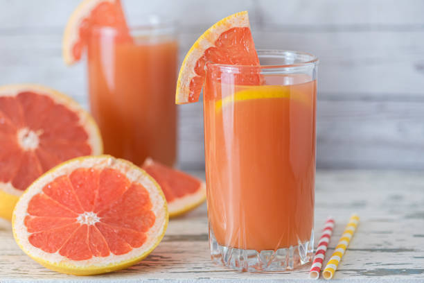 Grapefruit juice and ripe grapefruits on a light wooden background stock photo