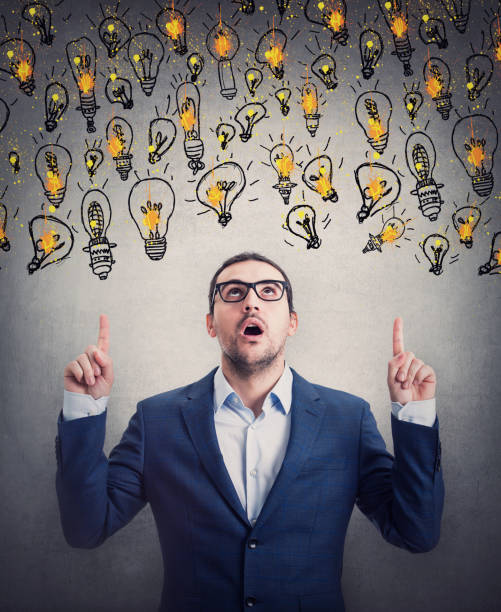 istock Amazed businessman pointing up index fingers, looking shocked as multiple light bulb float over his head. Impressed business person choosing from different creative ideas 1370858942