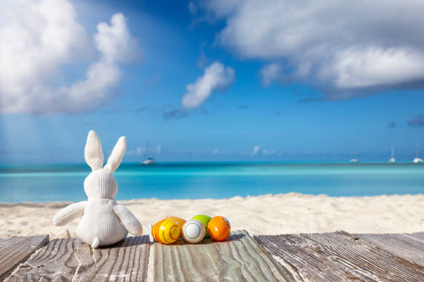 A easter travel concept with a white bunny and colorful eggs in front of a tropical paradise beach