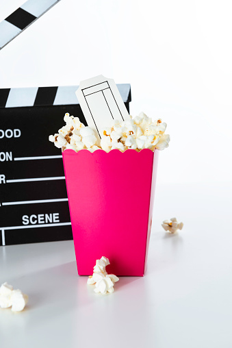 Movie clapper and pink popcorn bag with ticket in it with white background.