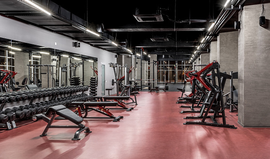 Exercise machines and racks with sets of black weights by the mirror in spacious, well lit, empty gym interior. Special equipment for physical training. Sport, fitness. Healthy lifestyle