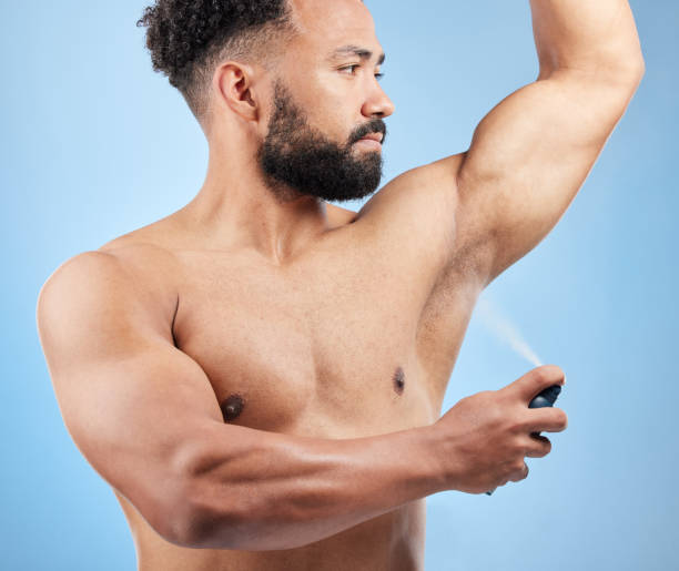 Studio shot of a handsome young man applying deodorant against a blue background