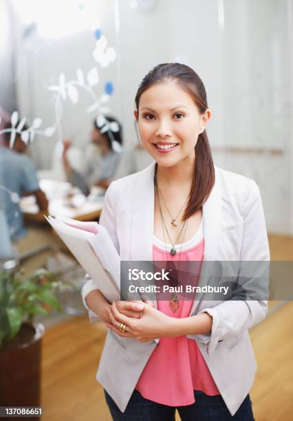 Portrait Of Smiling Businesswoman Holding Folders In Office Stock Photo - Download Image Now