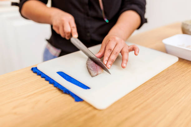 Female latin american cook preparing fish for lunch while standing in modern kitchen. Chef cutting fish with knife. Healthy lifestyle and food concept.