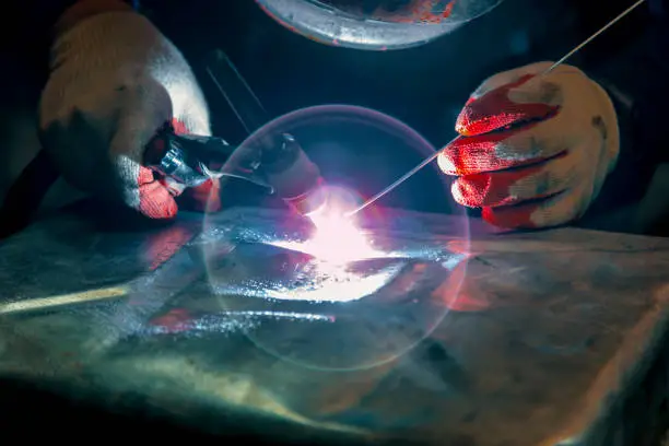 The welder ignites the arc and begins welding the aluminum canister with argon arc welding.