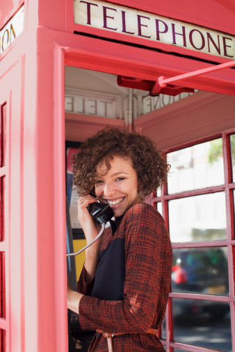 Old public telephone for making voice calls using coins or prepaid card stuck on a white wall. Person's hand holding handset to make a call.