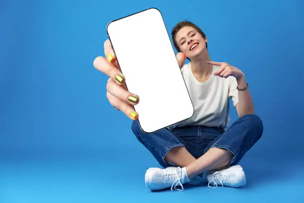 Happy woman shows blank smartphone screen against blue background, close up