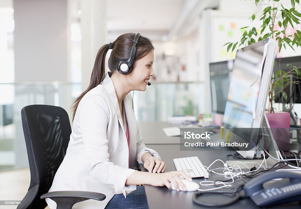 Donna d'affari con auricolare in ufficio utilizzando computer - Foto stock royalty-free di Ufficio