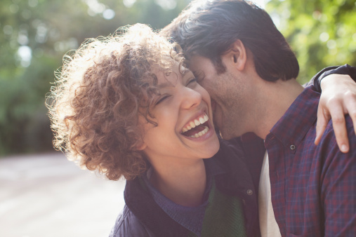 Close up of funny young caucasian couple laughing with their eyes closed and looking happy to be together while spending time at home. Loving smiling boyfriend embracing girlfriend from behind