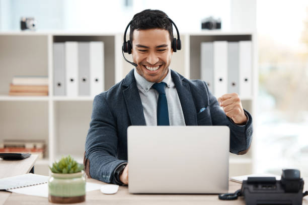 shot of a young male call center agent cheering while using a laptop in an office at work - excitement business person ecstatic passion imagens e fotografias de stock