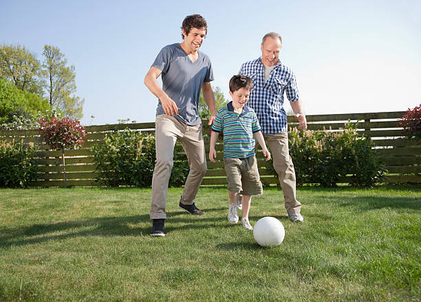 multi-generationen-familie fußball spielen im garten - grandparent multi generation family grandfather child stock-fotos und bilder