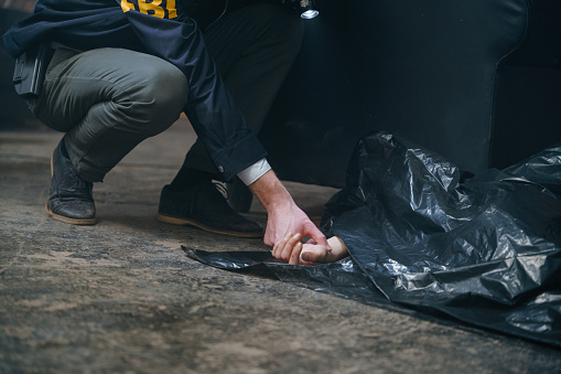 FBI agent checks the pulse on a female wrist, peeking out from under a black plastic bag