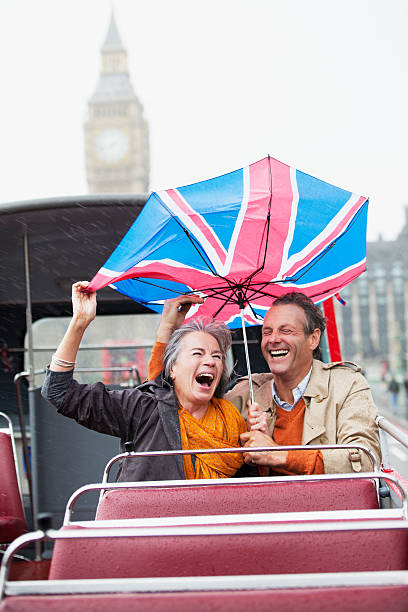 regen fallen auf paar mit britischer flagge regenschirm auf einem deck - front view bus photography day stock-fotos und bilder