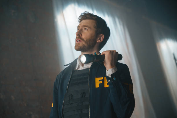 Concentrated FBI agent with a beard with a flash light at the crime scene looks up Concentrated FBI agent with a beard with a flash light at the crime scene looks up in a poorly lit abandoned storage room gun laws stock pictures, royalty-free photos & images