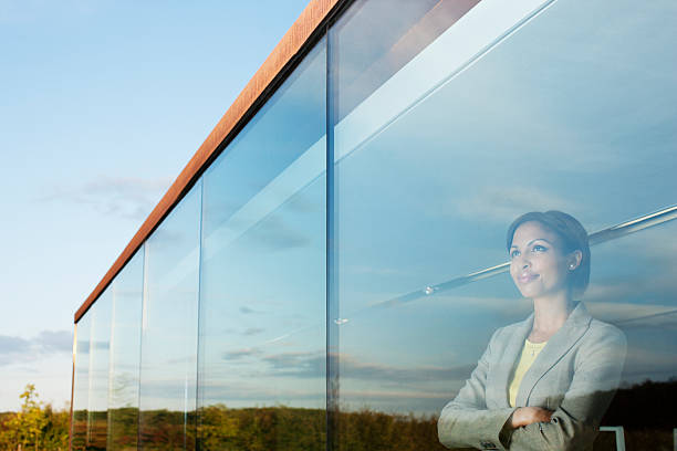 pensive businesswoman with arms crossed in office window - gelegenheid stockfoto's en -beelden