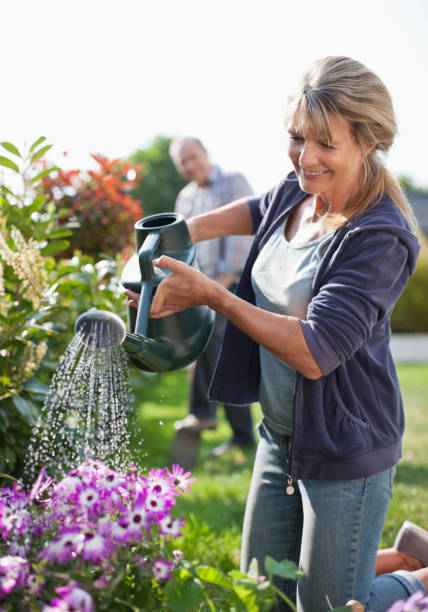 donna anziana che innaffia i fiori in giardino con annaffiatoio - gardening couple senior adult ethnic foto e immagini stock