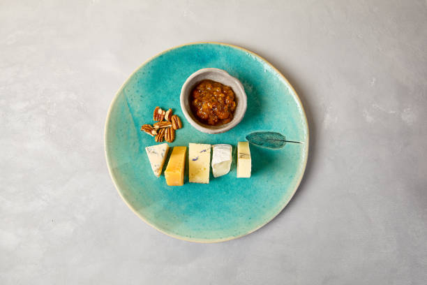 Cheese platter on blue ceramic plate. Cheeseboard on handmade dinner plate in modern style. Different cheese on ceramic dishware in minimal style