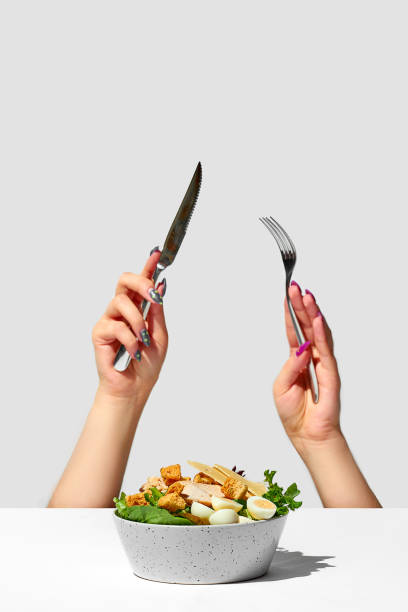 istock Caesar salad with croutons. A woman's hands with a knife and fork stick out from under the table. Creative 1370877822