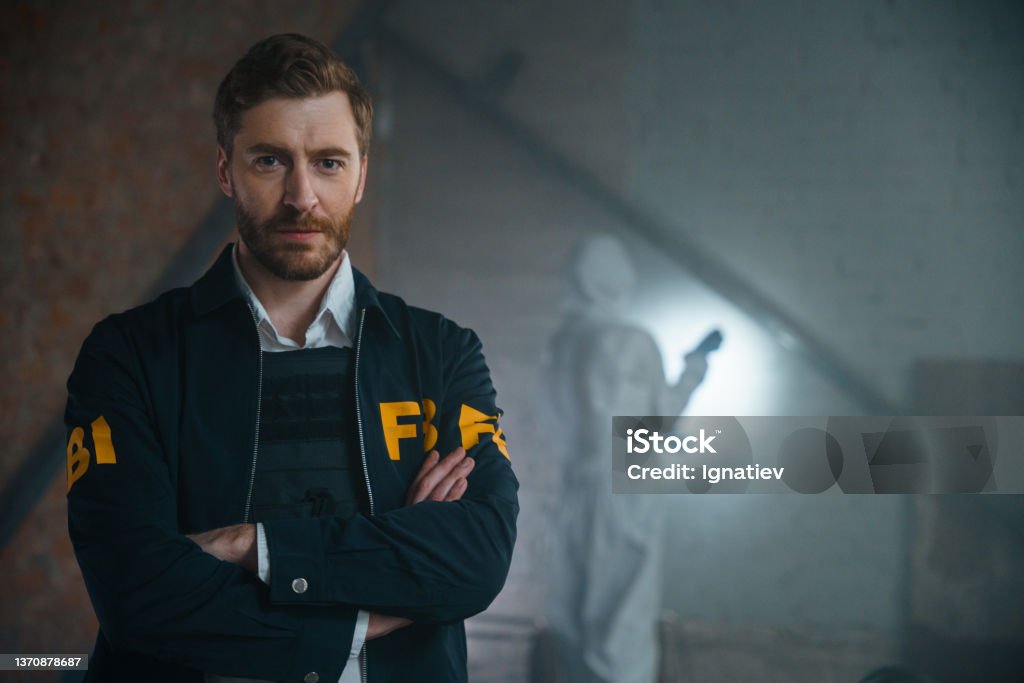 Handsome FBI agent standing with his arms crossed at the crime scene, he looks at camera, we see him from the waist up FBI Stock Photo