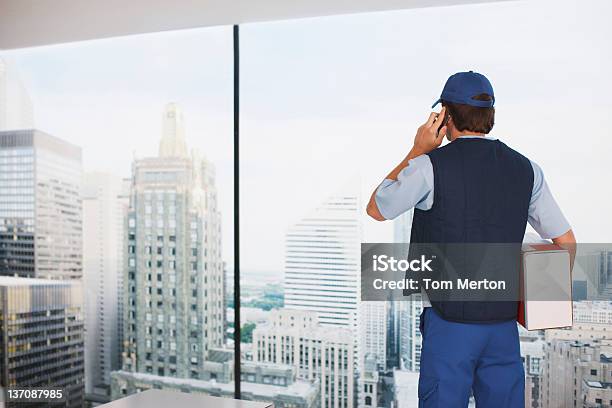 Deliveryman In Ufficio Con Il Pacchetto Parlare Sul Telefono Cellulare - Fotografie stock e altre immagini di Vista posteriore