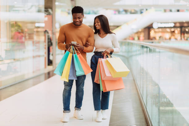 istock Happy black couple using phone walking with shopping bags 1370880426