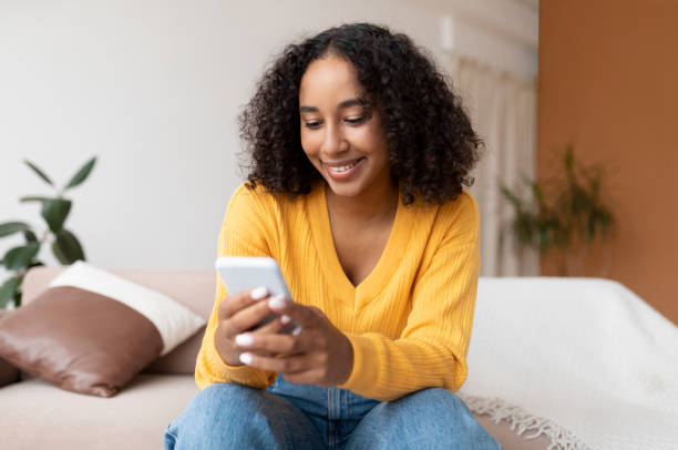 istock African American woman using mobile phone, having online video chat, sitting on couch, messaging in social media 1370880828