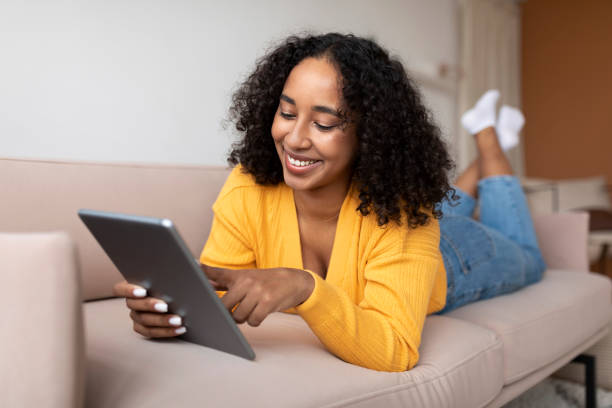 istock Relaxed young black woman lying on couch and using tablet pc, chatting online or checking social media 1370880928
