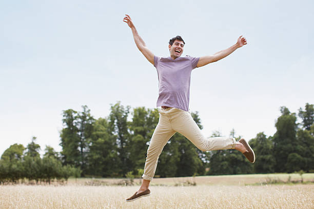 homem pulando na zona rural exuberante campo - braços no ar - fotografias e filmes do acervo