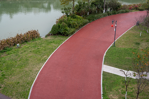 The red asphalt runway in the park is flanked by trees.