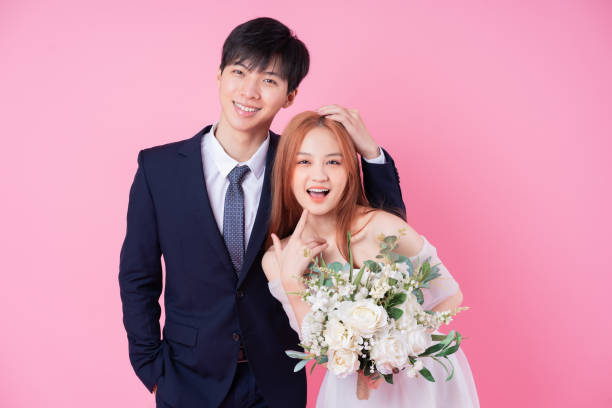istock Young Asian bride and groom posing on pink background 1370884549
