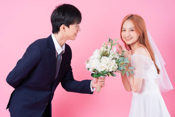 istock Young Asian bride and groom posing on pink background 1370884553