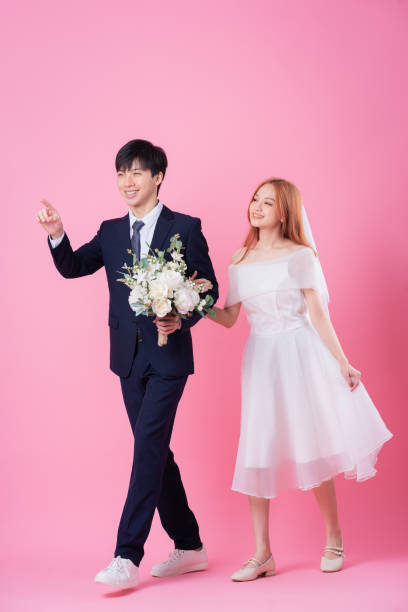 istock Young Asian bride and groom posing on pink background 1370884560