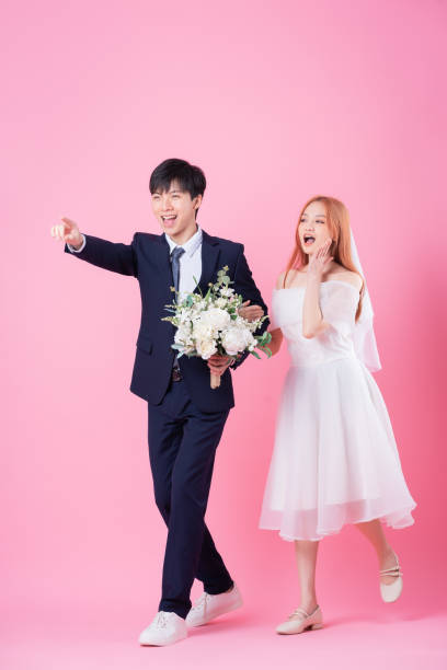 istock Young Asian bride and groom posing on pink background 1370884572