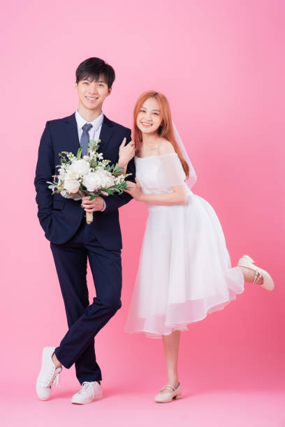 istock Young Asian bride and groom posing on pink background 1370884576