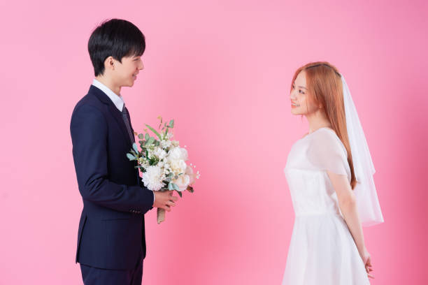 Young Asian bride and groom posing on pink background