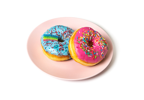 Two multi-colored donuts with a rainbow lie on a pink plate on a white background.