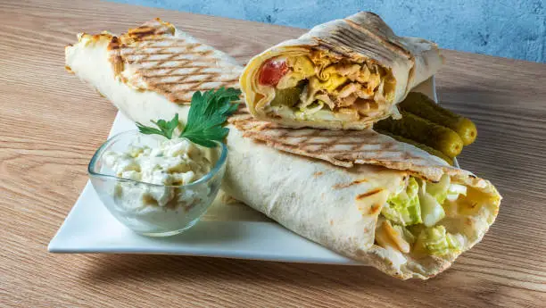 Shawarma chicken roll. Fresh roll of thin lavash or pita bread filled with grilled meat, cheese, cabbage, carrots, sauce, green. Traditional Eastern snack.