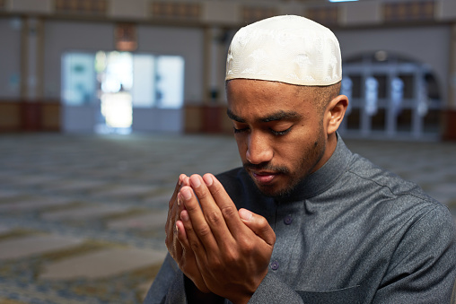 Portrait of a young Muslim man making dua and praying in a mosque