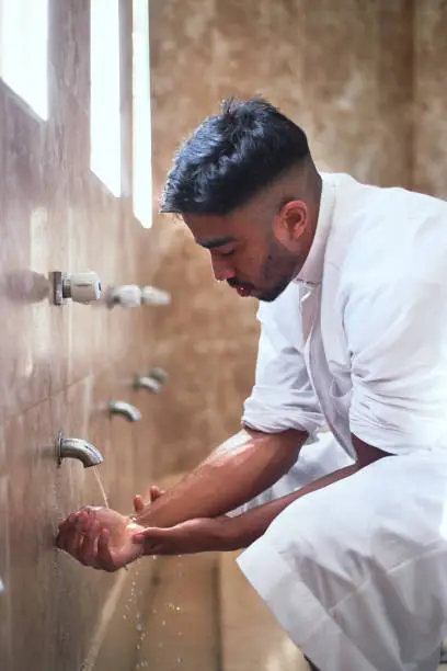 A young Muslim man performs wudu during prayers at a mosque by cleansing his face with water in the washroo