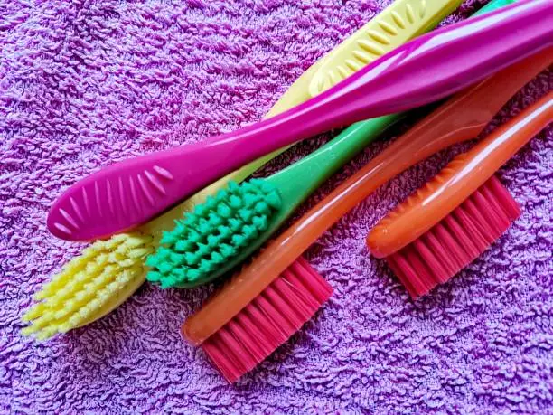 Photo of Five toothbrushes of different colors lying optionally on a purple towel.