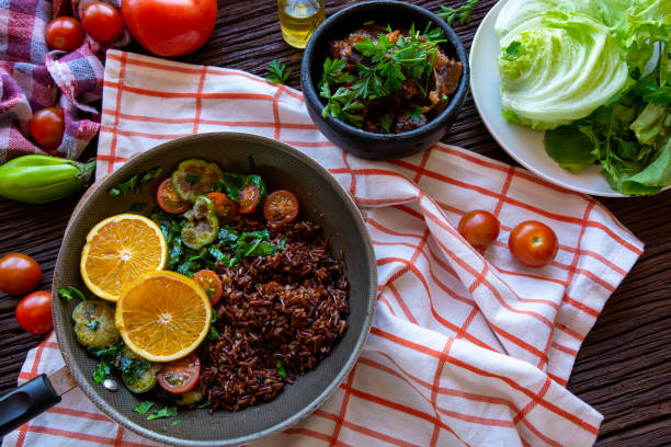 istock Pan Cook with red rice, tomatoes, lettuce, meat on a rustic wood table. 1370891096