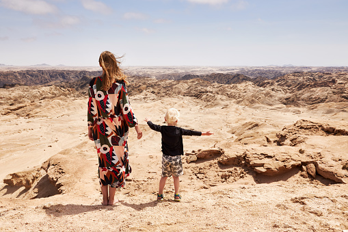 A woman in a beautiful dress stands with her little son on vacation in Namibia in front of the lunar landscape in the Erongo area and enjoys the view