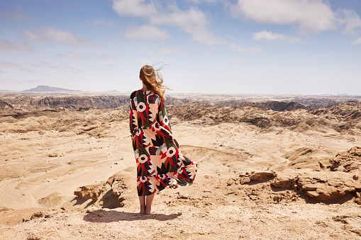 A woman in a beautiful dress stands in front of the lunar landscape in the Erongo region on vacation in Namibia