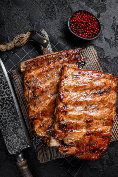 istock Stack of grilled pork ribs in BBQ sauce on a chopping board. Black background. Top view 1370891924