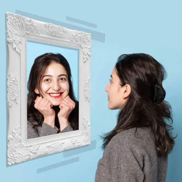 Photo of Smiling young girl looking at mirror isolated on light background. Contemporary art collage. Concept of emotions, inner world, mental health